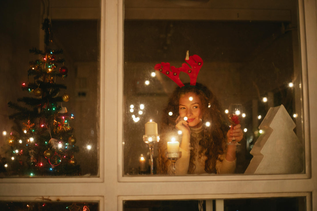 Woman looking out window with glass of wine at Christmas